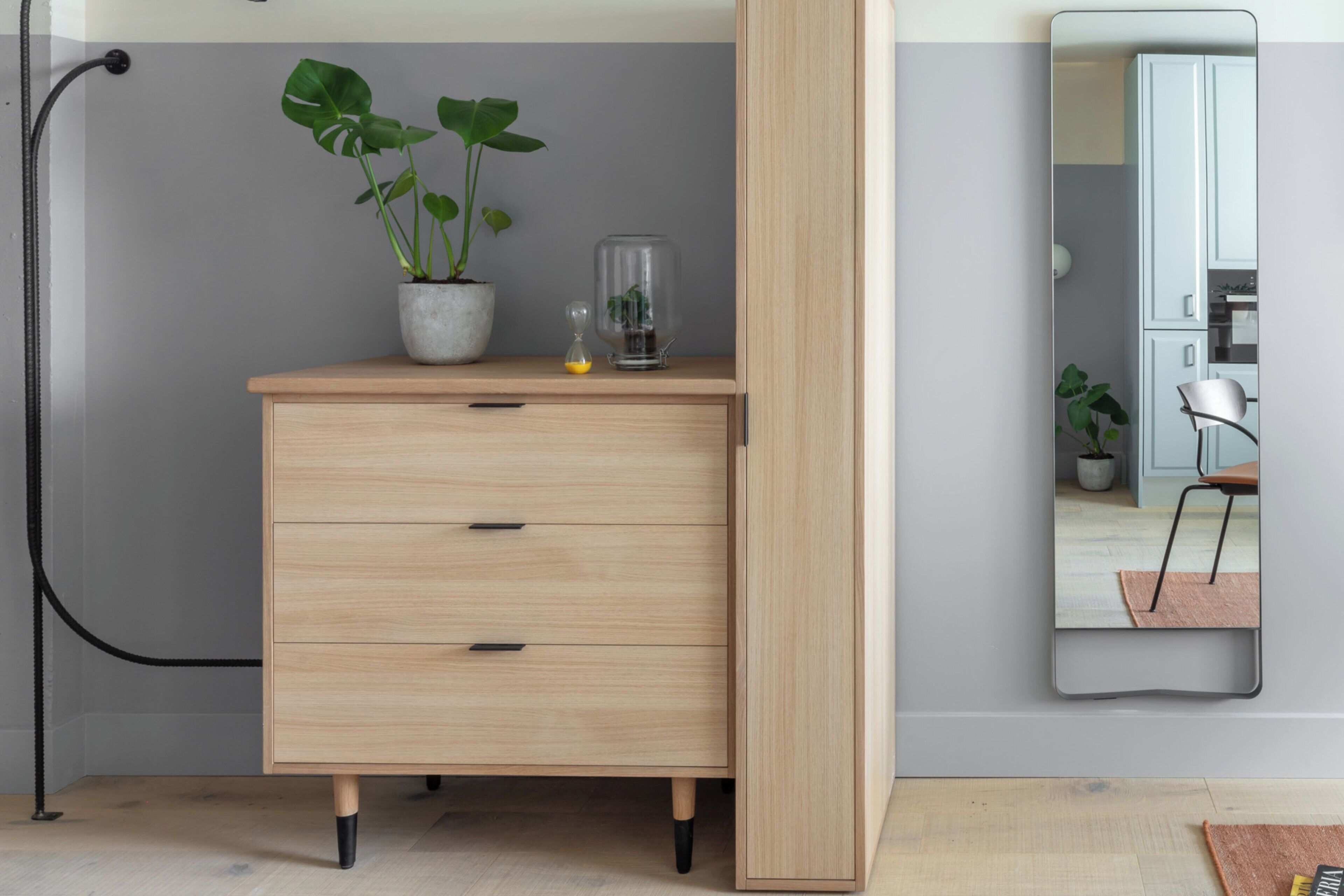 A wooden dresser with drawers, a potted plant, and a glass container on top.