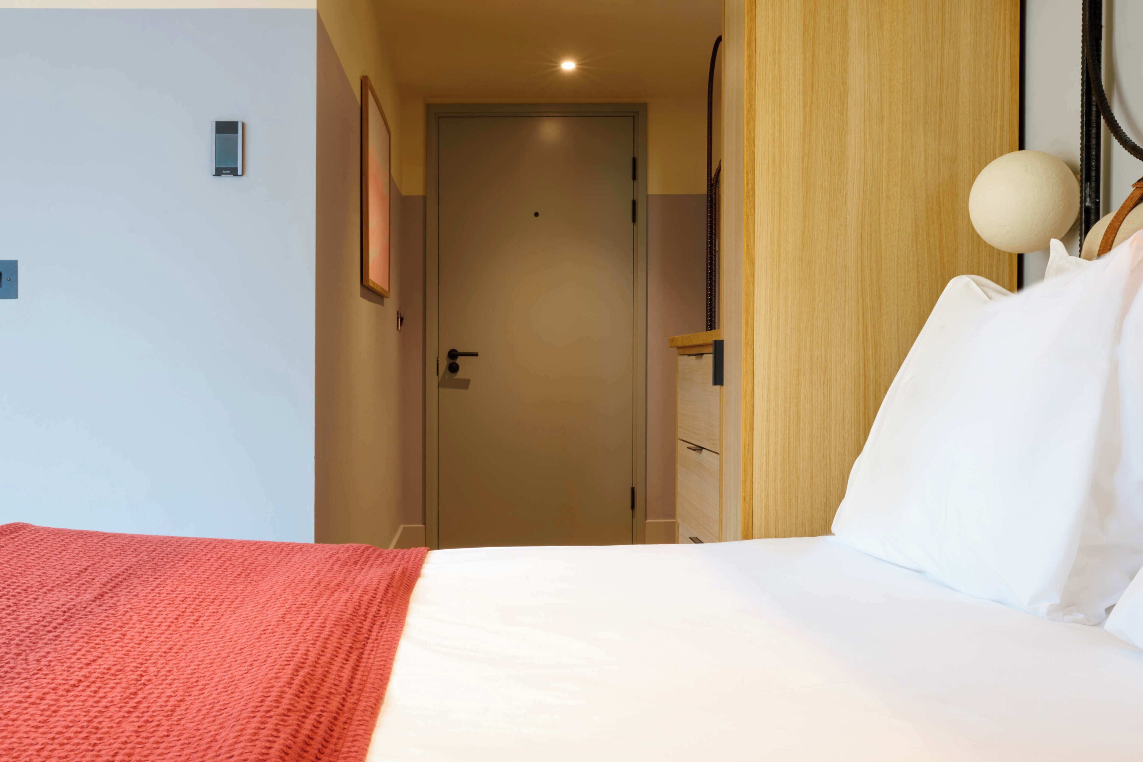 Une chambre d’hôtel avec un lit, une porte, un luminaire fixé au mur et un panneau en bois.