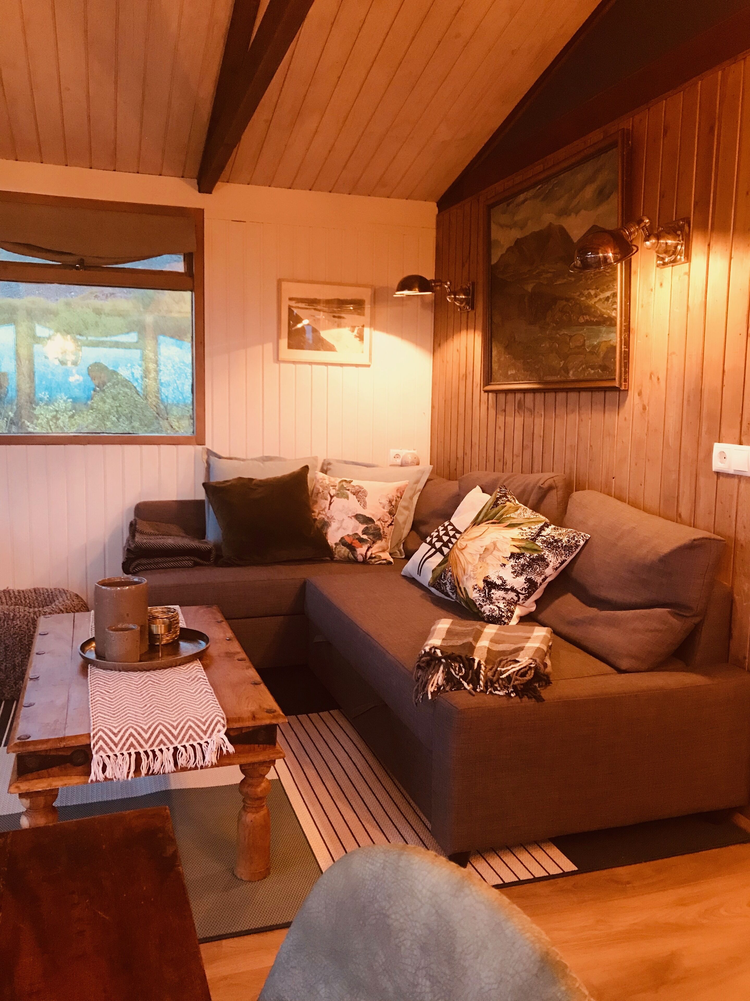 Una sala de estar acogedora con techo de madera, un sofá con cojines, una mesa de centro con bandeja y velas, y una ventana con vistas a zonas verdes.