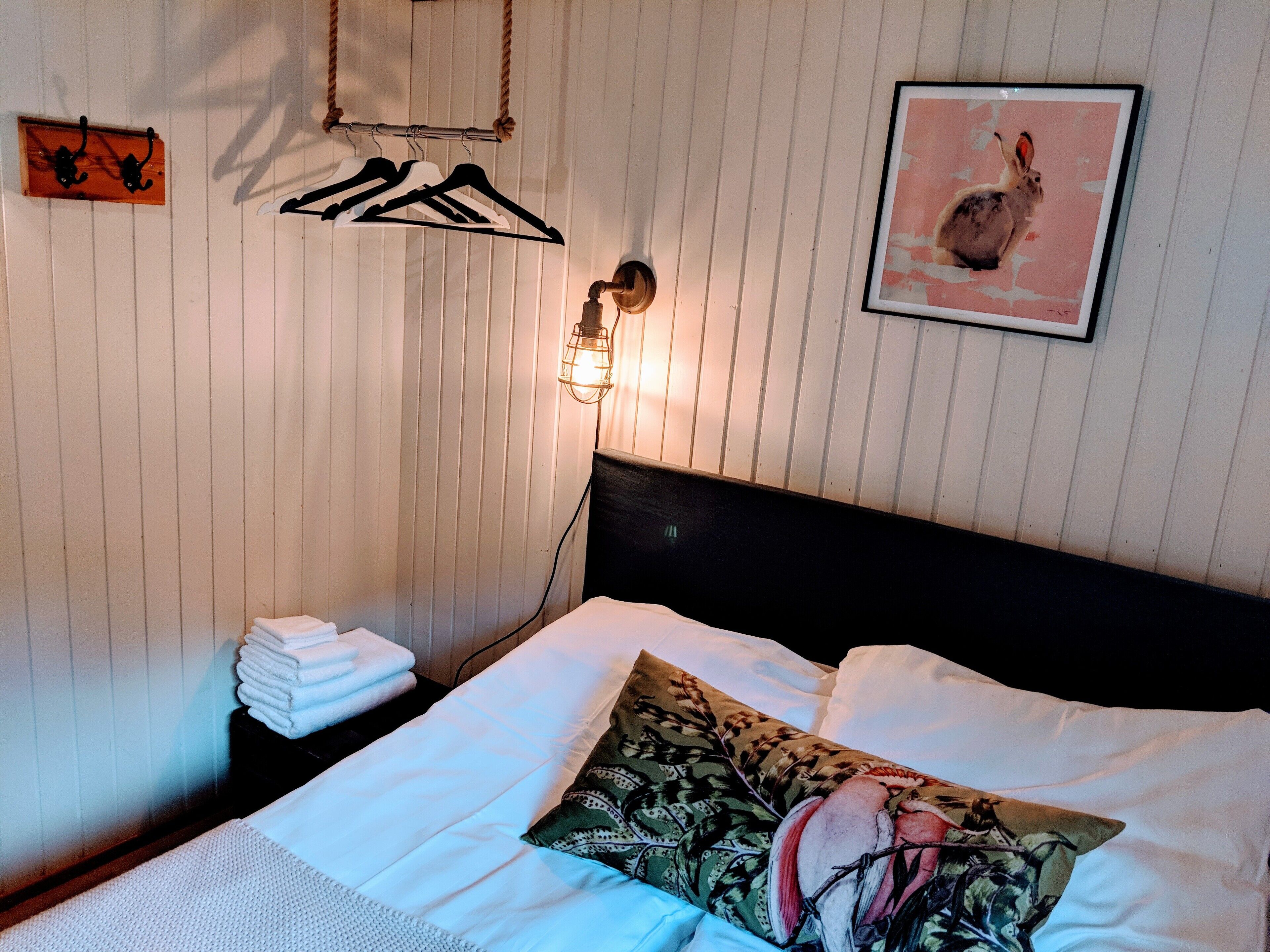 A neatly made bed with a patterned pillow, a stack of folded towels, and a wall-mounted light fixture.