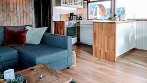 A modern kitchen with wooden cabinets, a built-in oven, and a central island. - Múlakot Cosy Cabins (Borgarbyggd)
