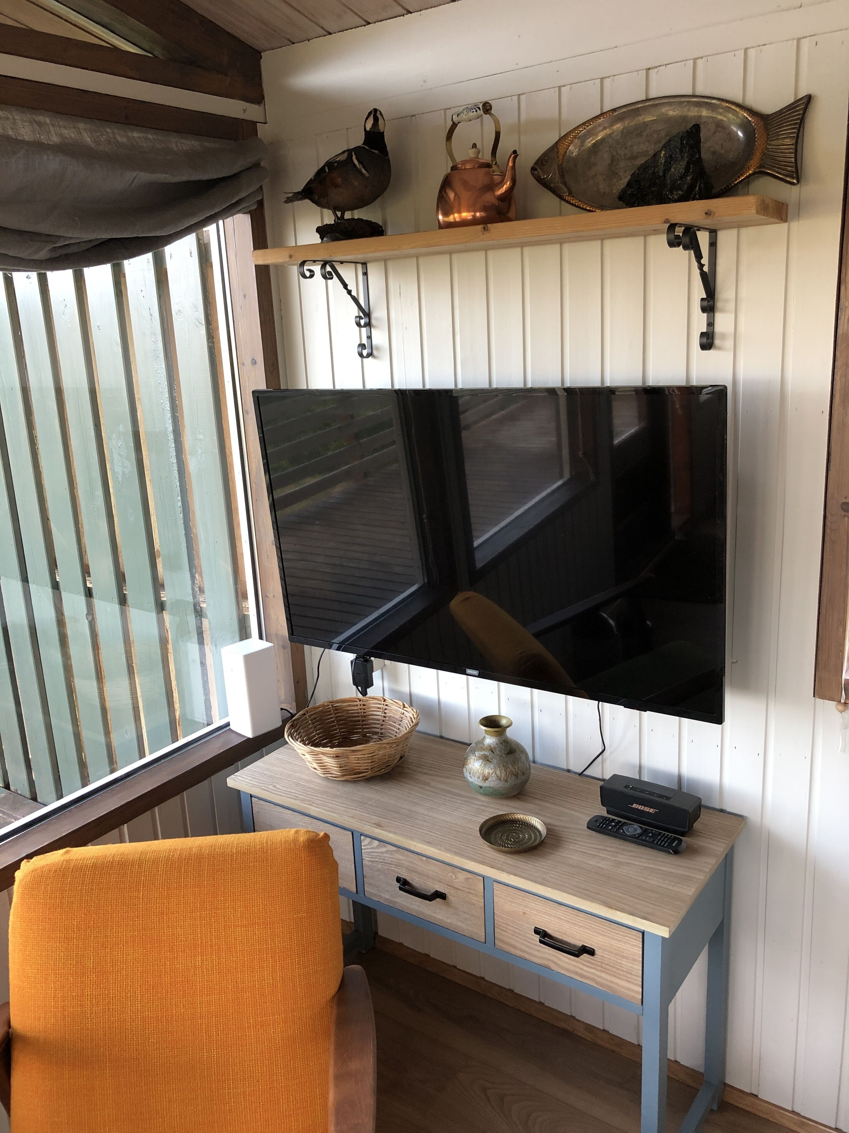 Une pièce confortable avec un bureau en bois, une télévision et une fenêtre équipée de stores.