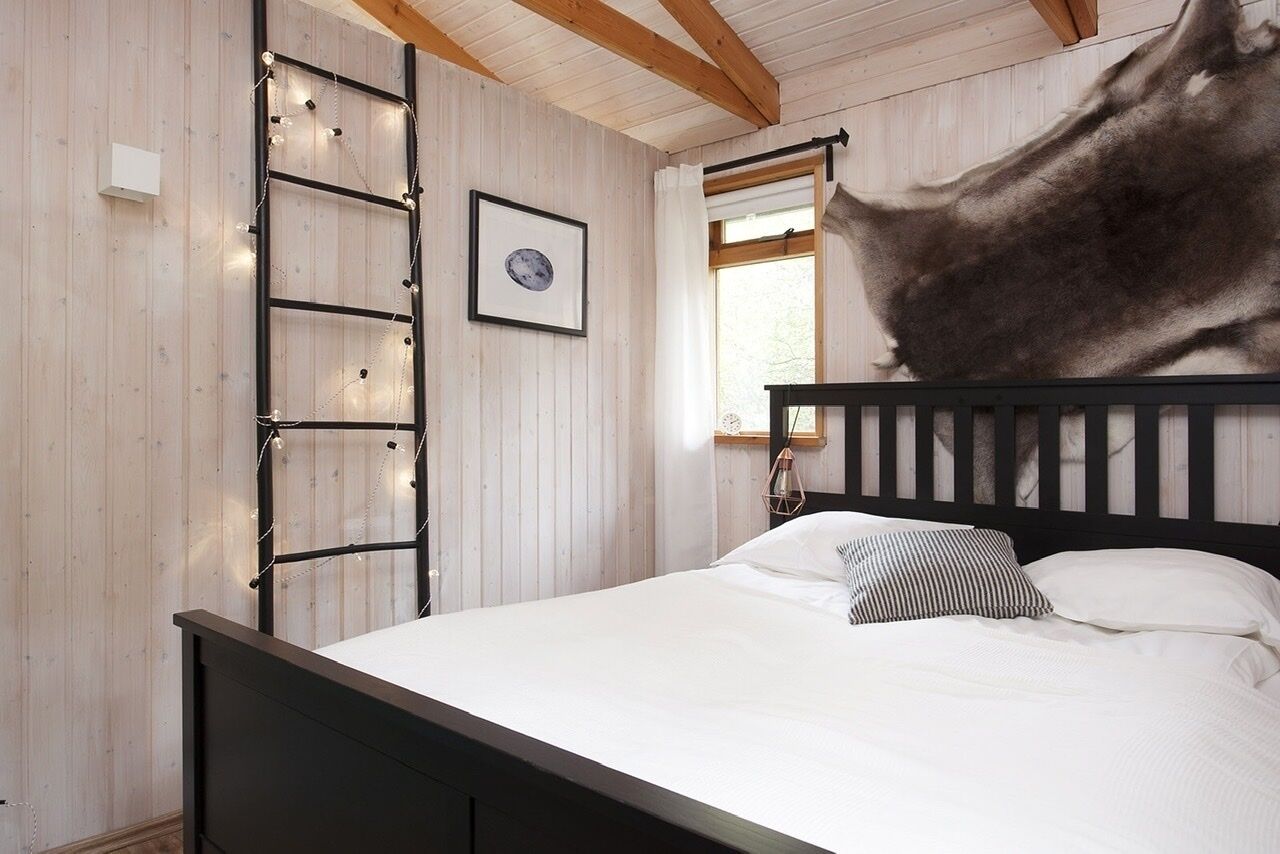 Een slaapkamer met een houten sprokelatuur, een ingelijst schilderij, een bed met witte beddengoed en een raam met gordijnen.
