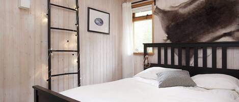 Een slaapkamer met een houten sprokelatuur, een ingelijst schilderij, een bed met witte beddengoed en een raam met gordijnen.