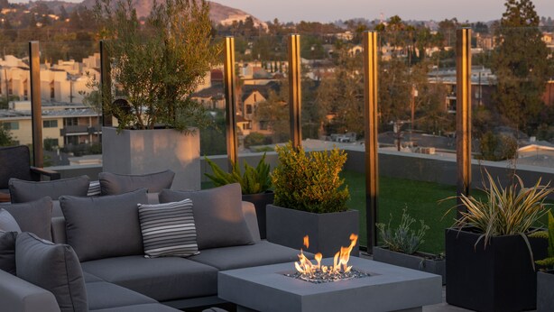 A modern outdoor seating area with a fire feature, grey sofas, and planters. - The Glenmark, Glendale, a Tribute Portfolio Hotel (Glendale)
