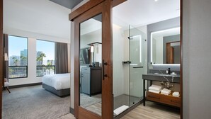 A modern hotel room with a large bed, a walk-in closet, a glass shower, and a city view. - The Glenmark, Glendale, a Tribute Portfolio Hotel (Glendale)