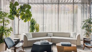 A modern living room with a sectional sofa, two coffee tables, and several potted plants. - The Glenmark, Glendale, a Tribute Portfolio Hotel (Glendale)