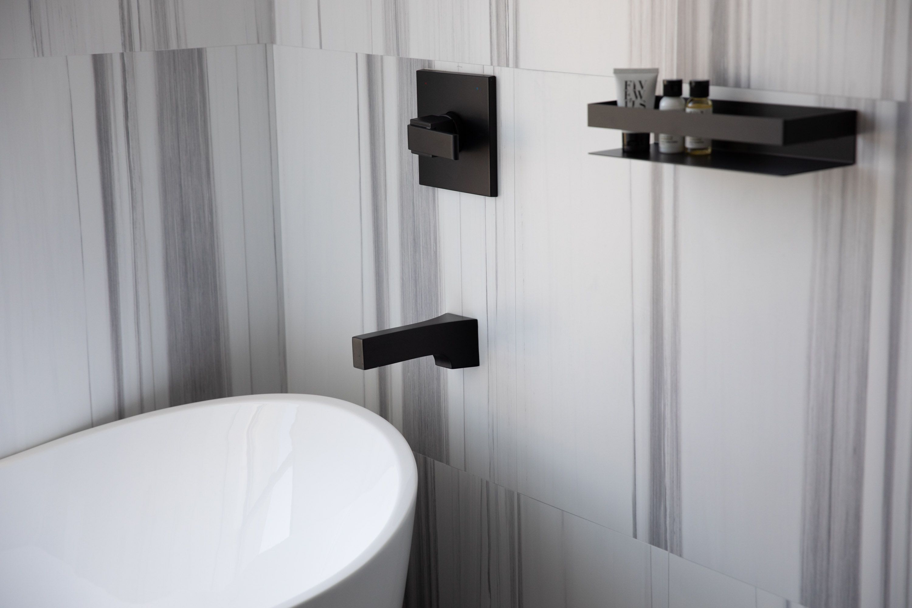 Un bagno moderno con un lavandino bianco, accessori neri e una parete con effetto marmo.