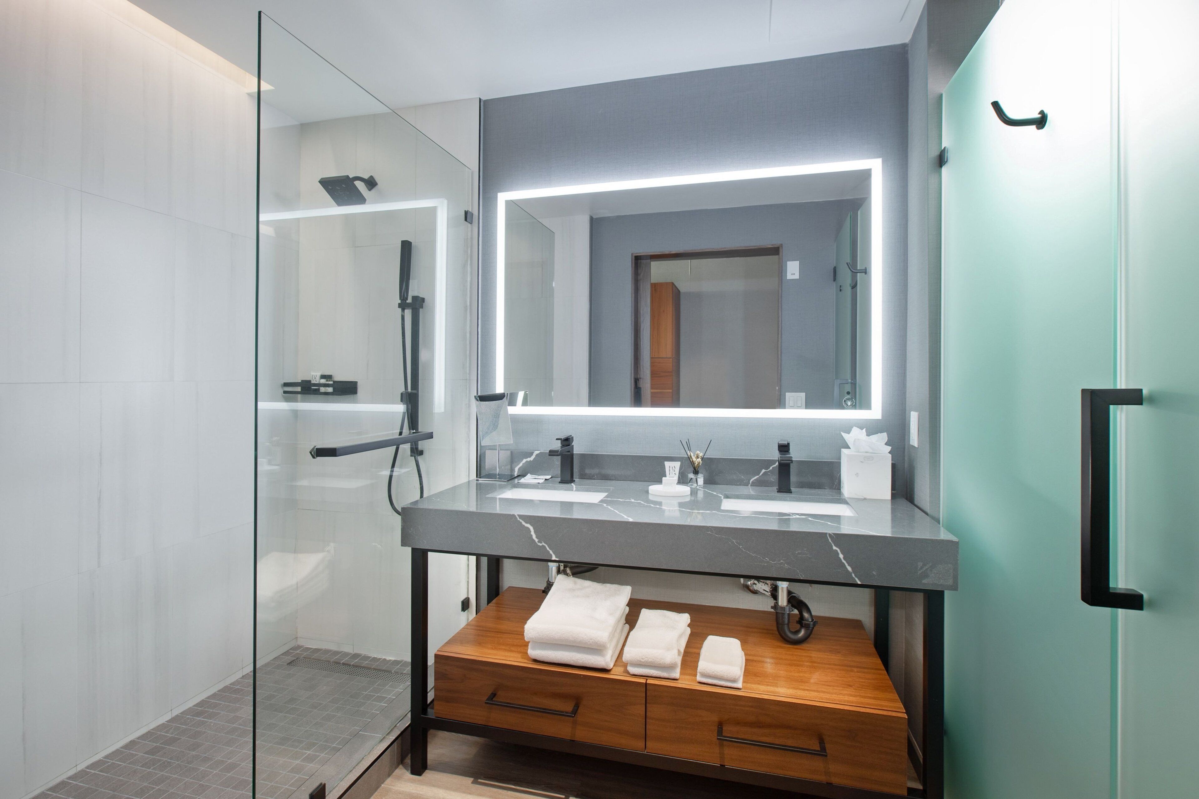 Un baño moderno con ducha envuelta en vidrio, tocador de mármol y banco de madera con toallas.