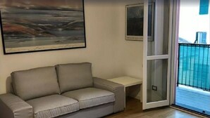 Ein Wohnzimmer mit grauem Sofa, einem kleinen Tisch und einer Schiebeglastür, die auf einen Balkon führt.