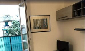 A room with a large window, a framed picture on the wall, and a TV stand.