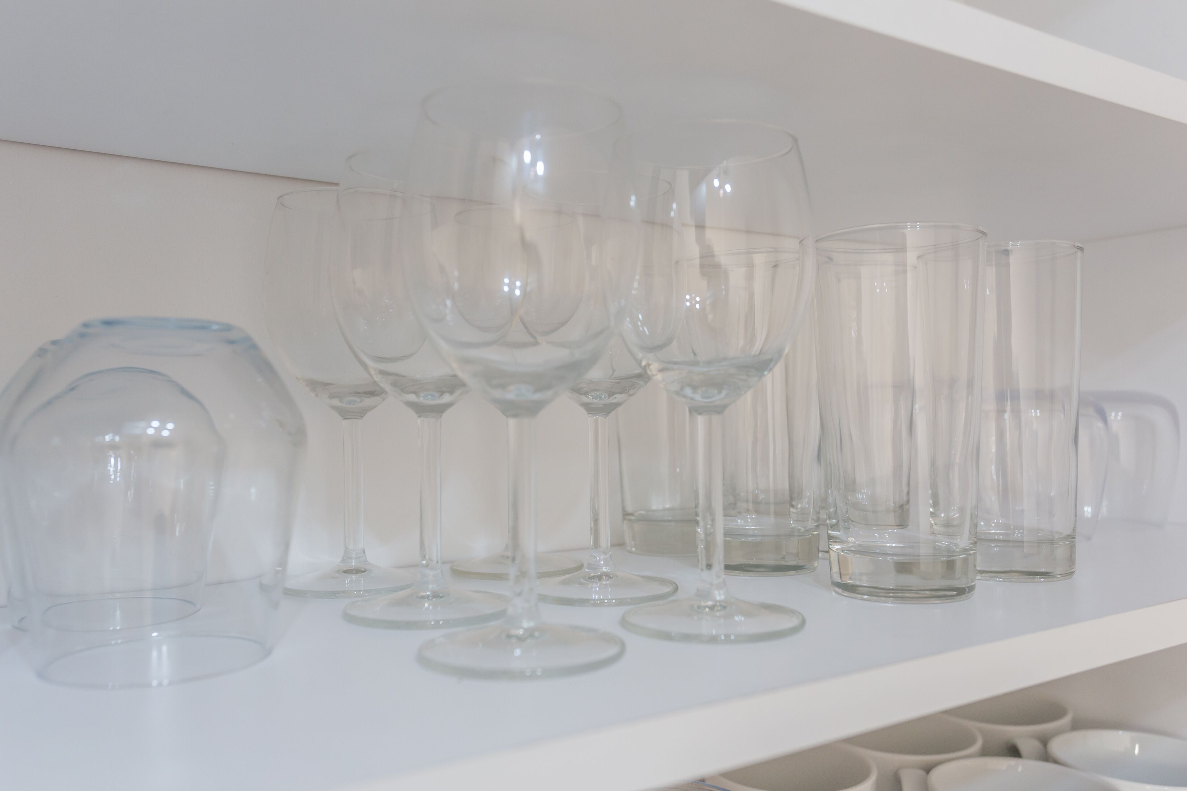 Une étagère blanche sur laquelle sont disposés divers objets en verre transparent, notamment des verres à vin et une théière.