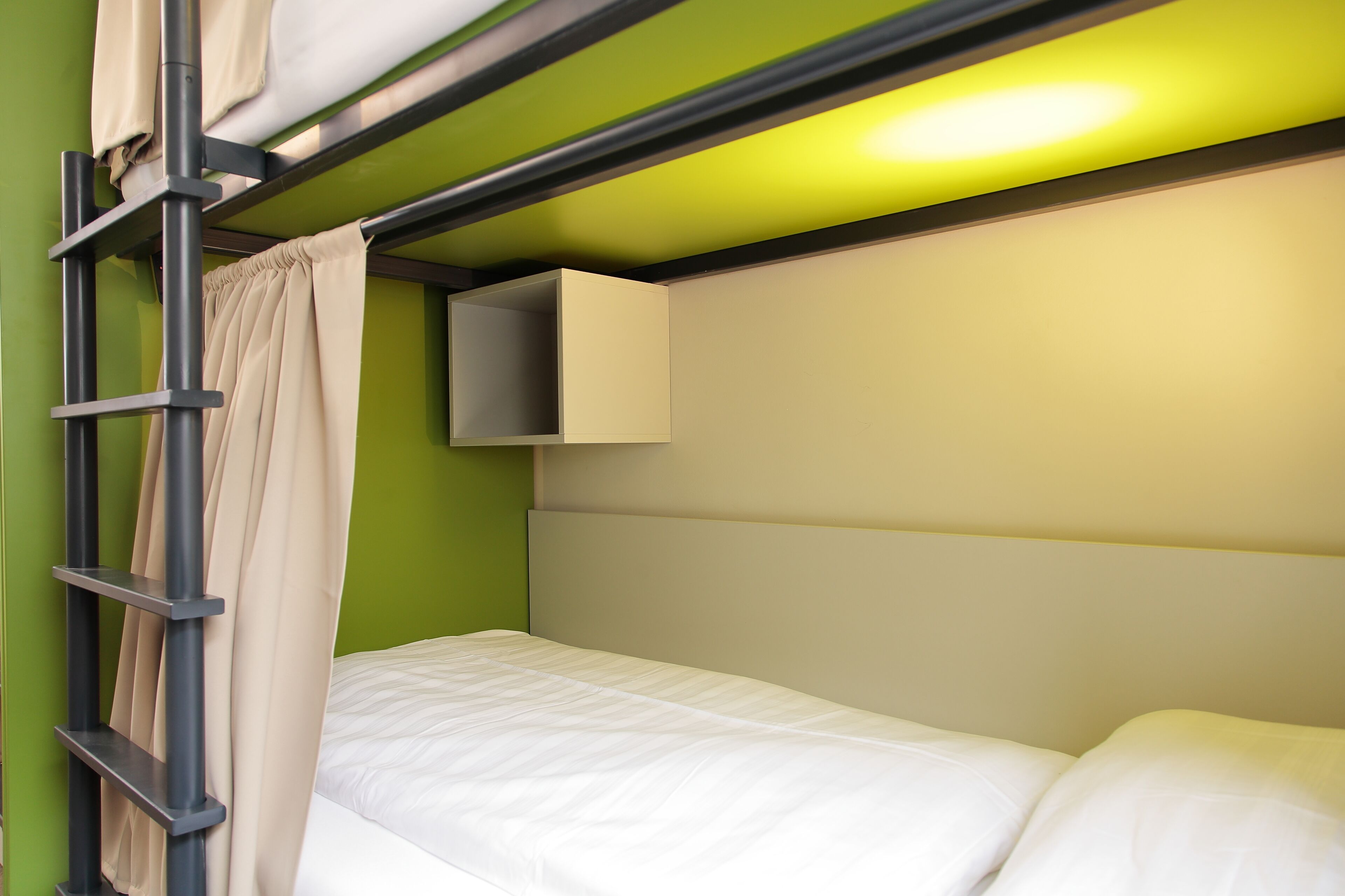 Una cama litera con escalera, un archivador pequeño y una pared verde.