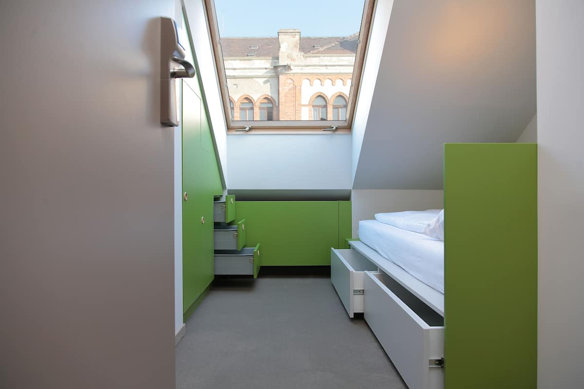 Une petite chambre à coucher moderne, dotée d’un puits de lumière, de meubles de rangement verts et d’un lit.