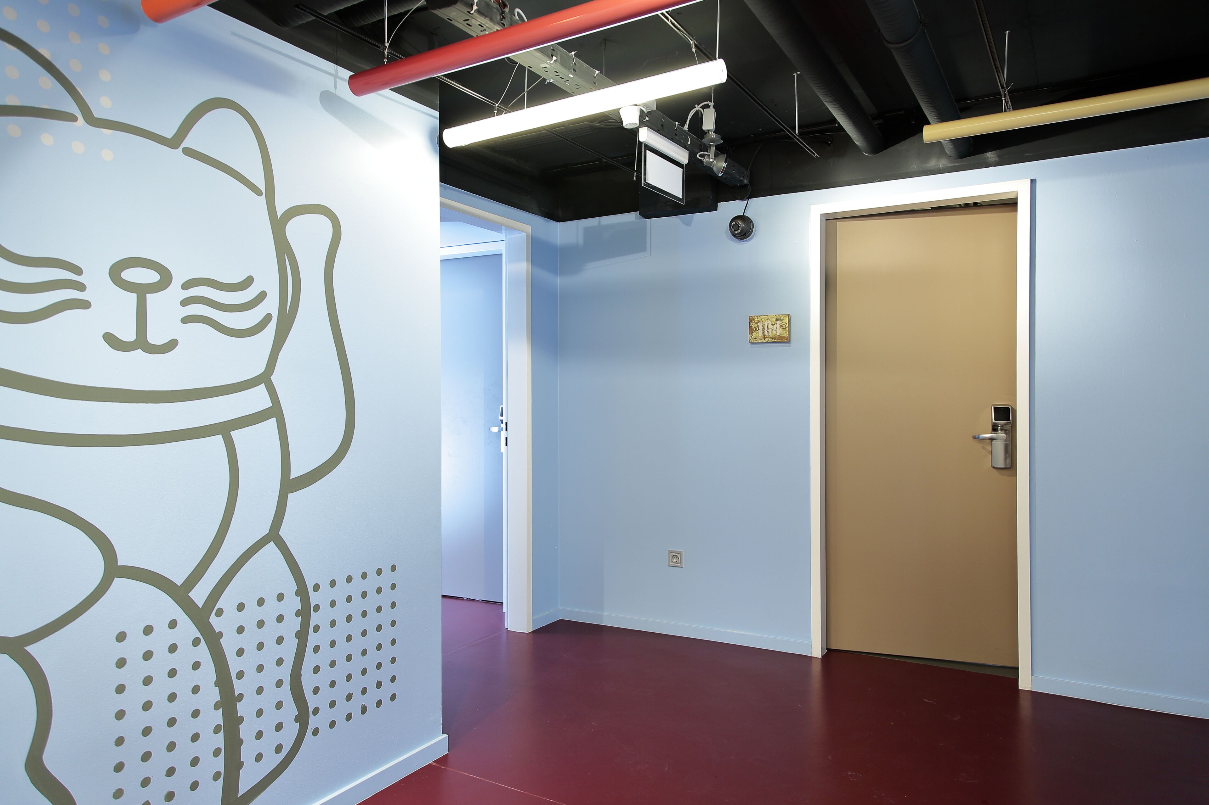 Un pasillo con piso rojo, una puerta color beige y un muro con el contorno de un gato.