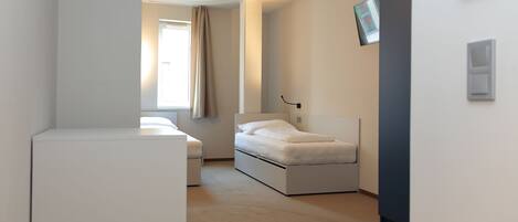 Un dormitorio moderno y minimalista con cama, un escritorio pequeño y una ventana con cortinas.