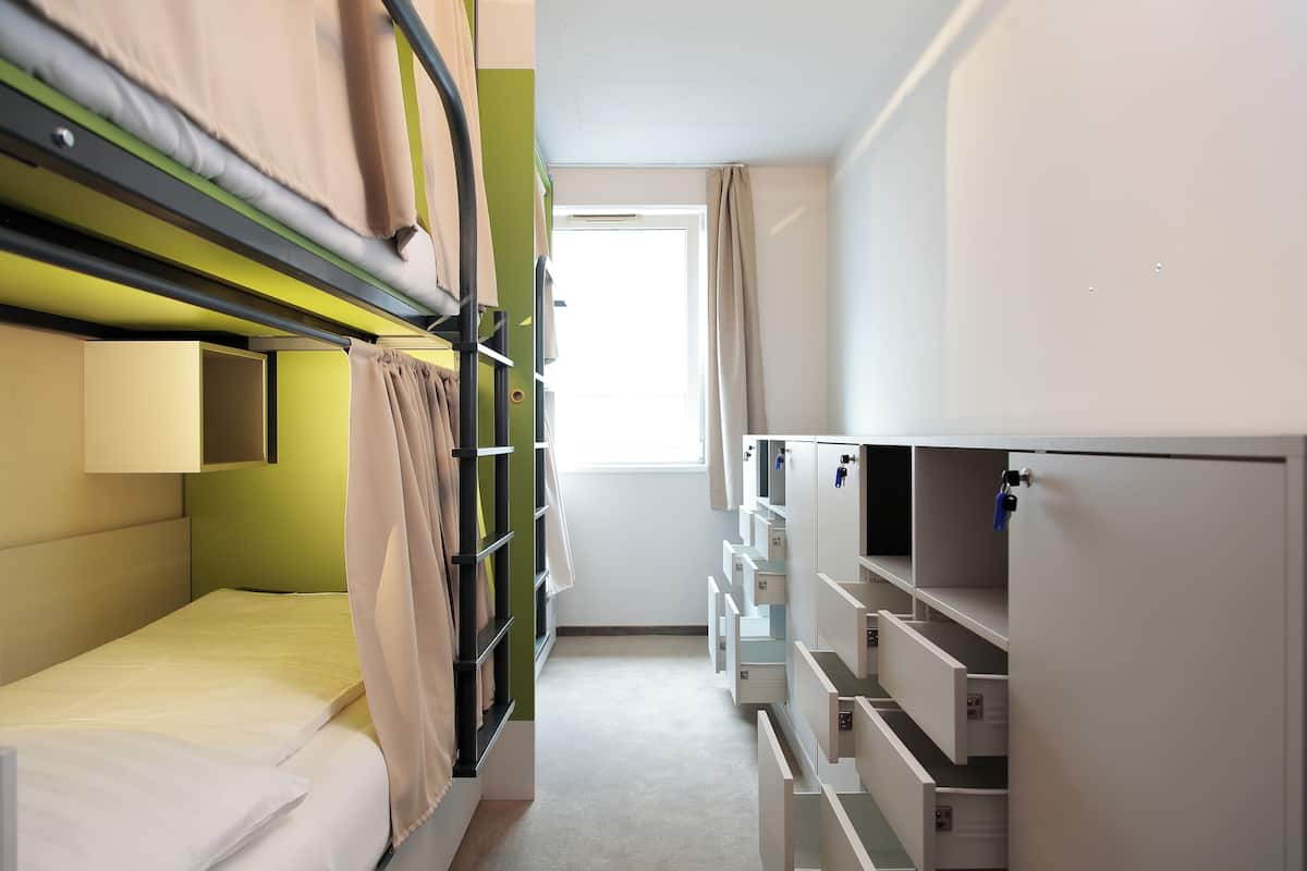 Une chambre d’hôtel compacte avec des lits superposés, un petit bureau et une armoire avec plusieurs compartiments.