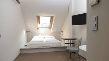 Une petite pièce bien éclairée, avec un lit, une chaise, une petite table et une fenêtre avec des rideaux.