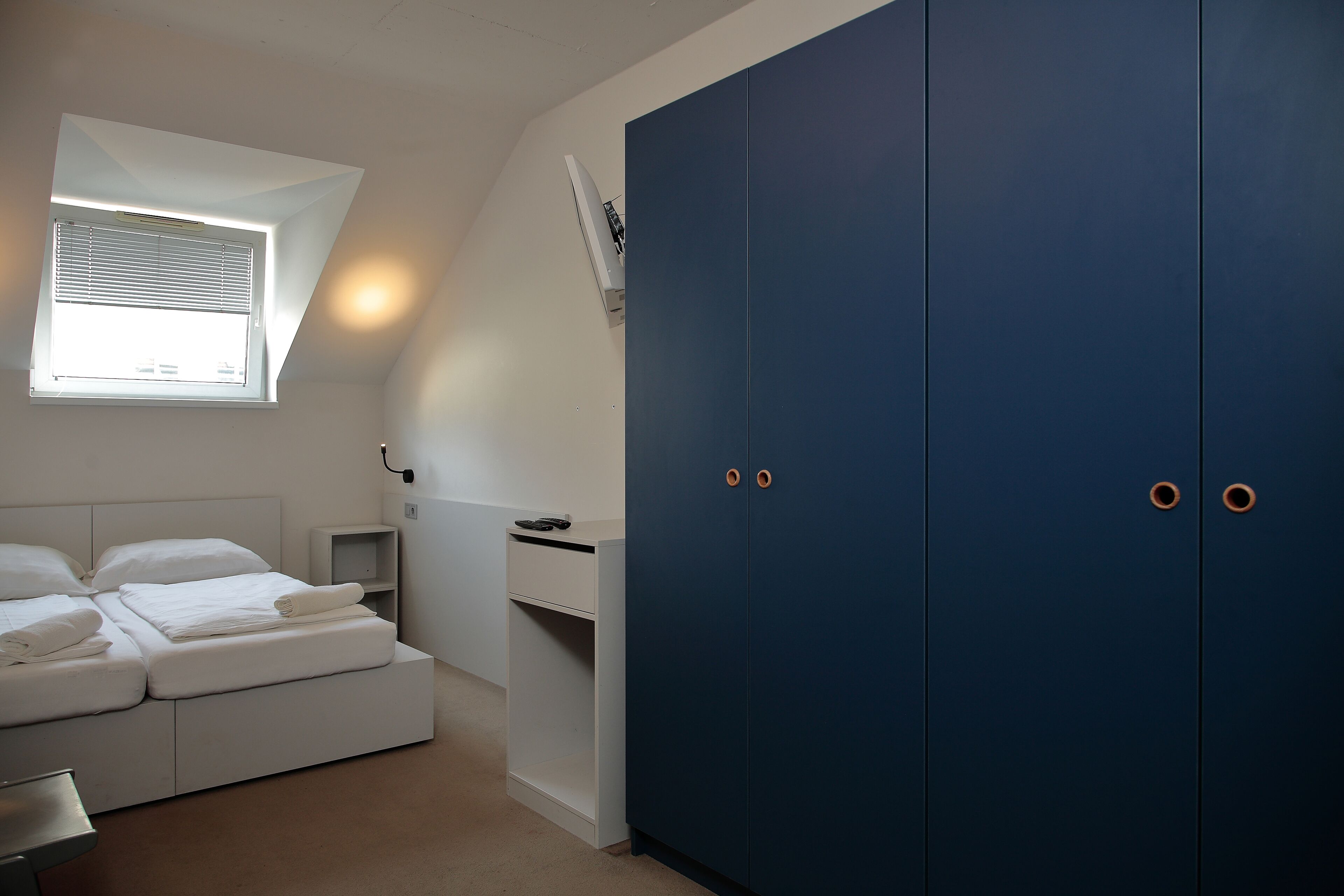 A bedroom with a bed, a wardrobe, a desk, and a window.