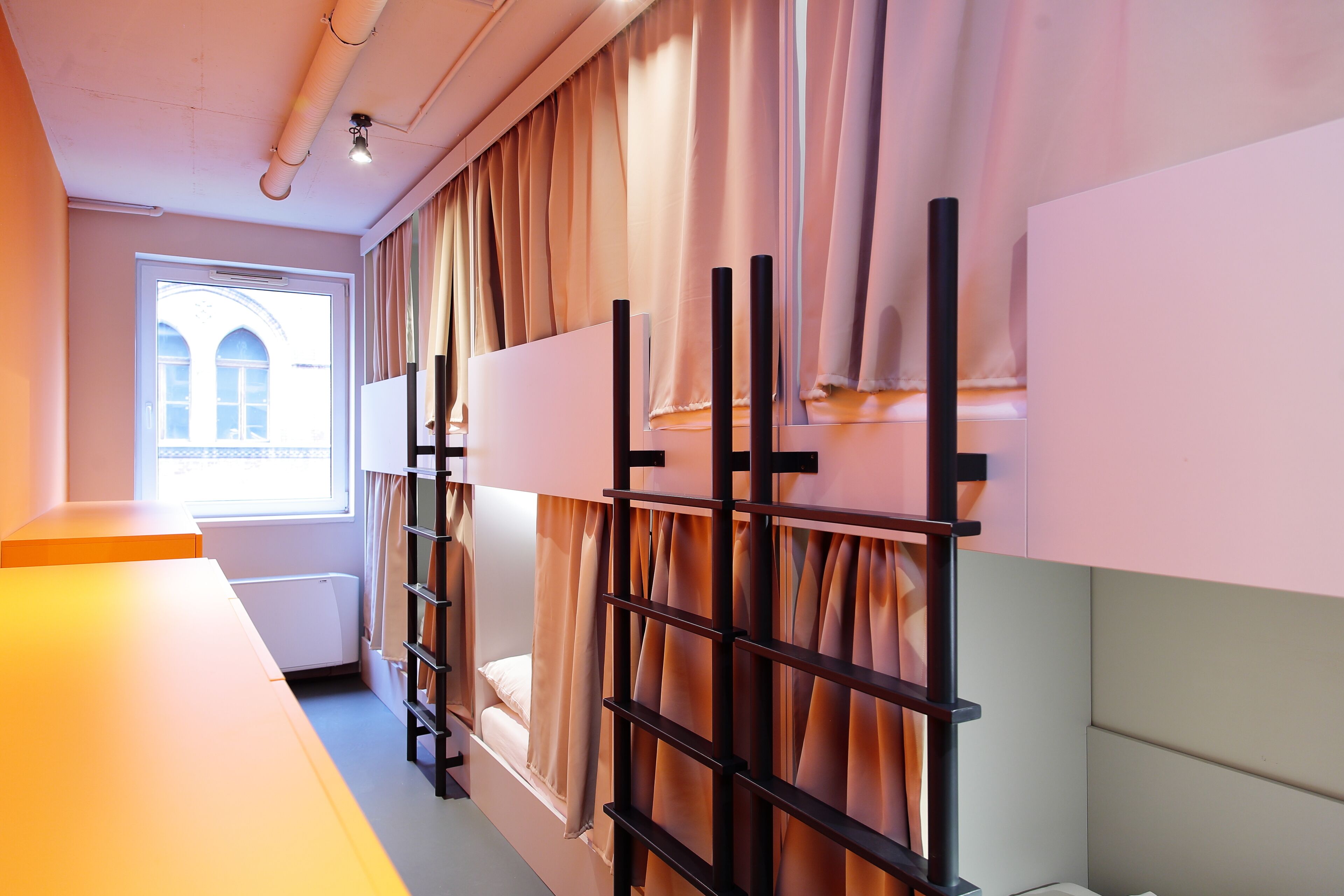 Habitación de hotel con literas, una ventana con cortinas, un radiador y una pared blanca.