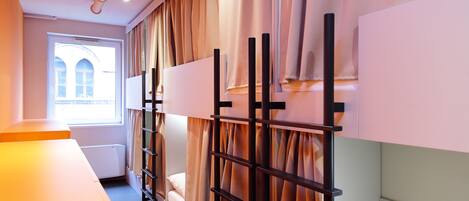 Habitación de hotel con literas, una ventana con cortinas, un radiador y una pared blanca.