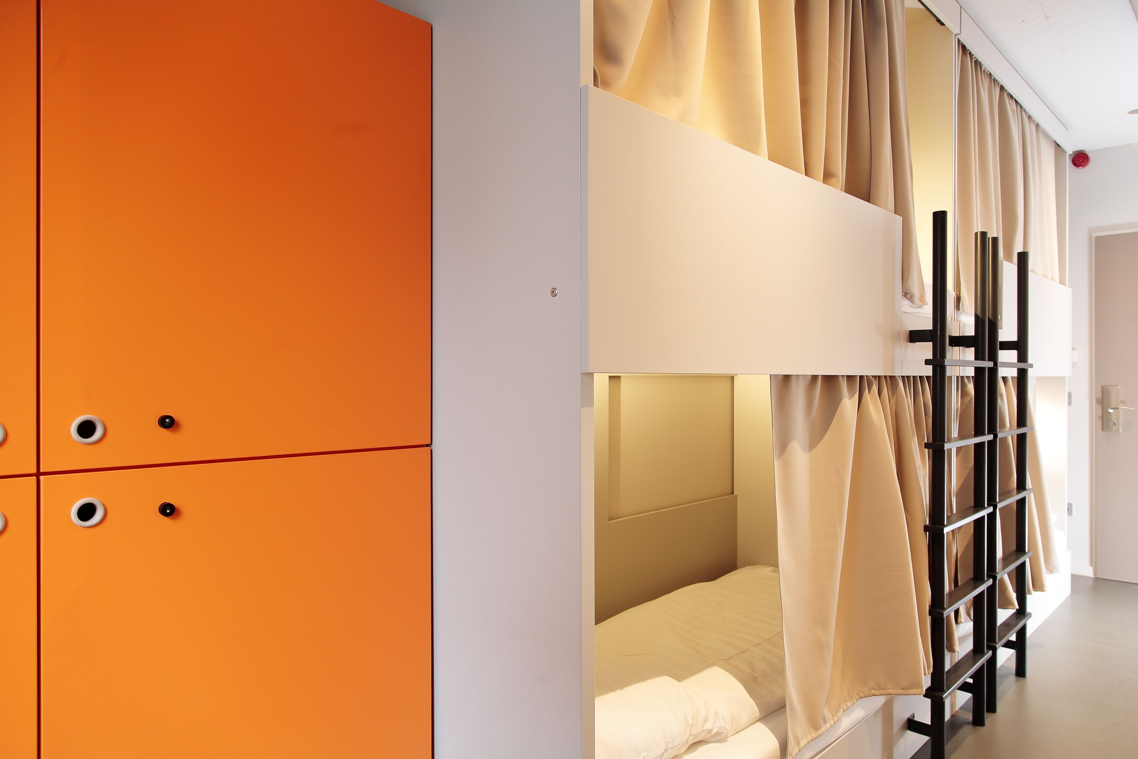 A bunk bed with beige curtains, an orange wardrobe with circular handles, and a white door in a hotel room.