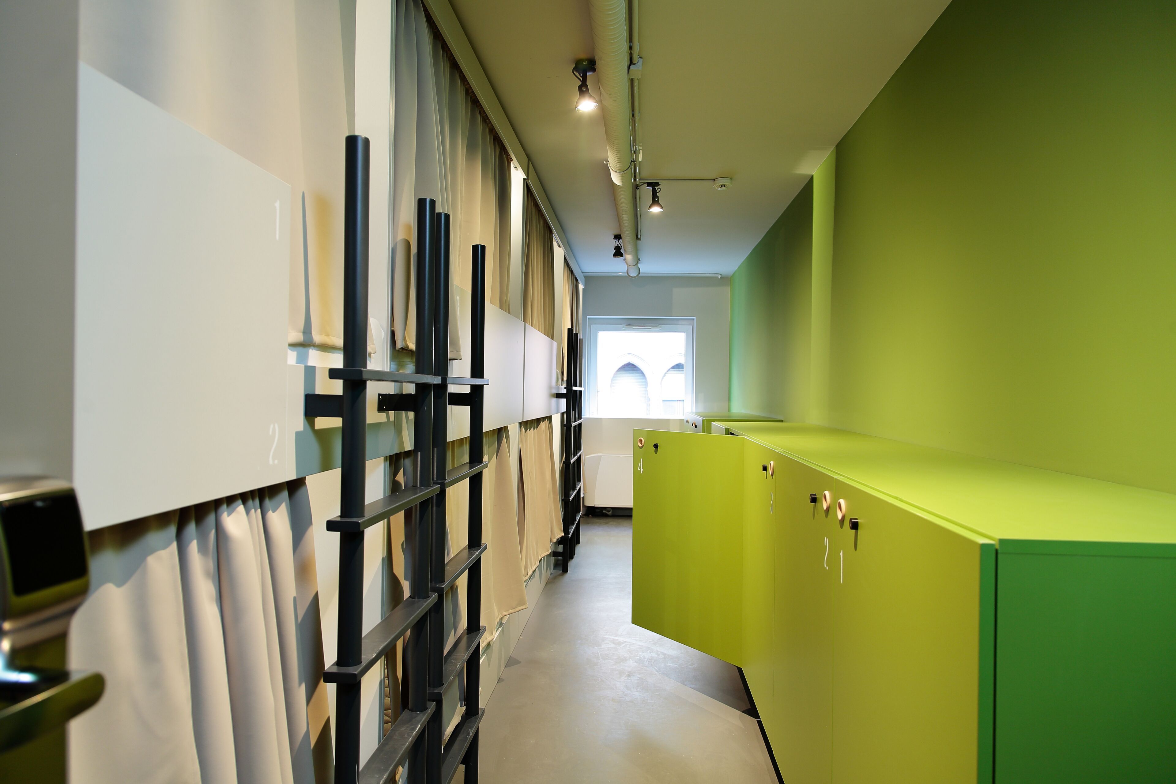 A corridor with bunk beds, a green storage unit, and a window with natural light.