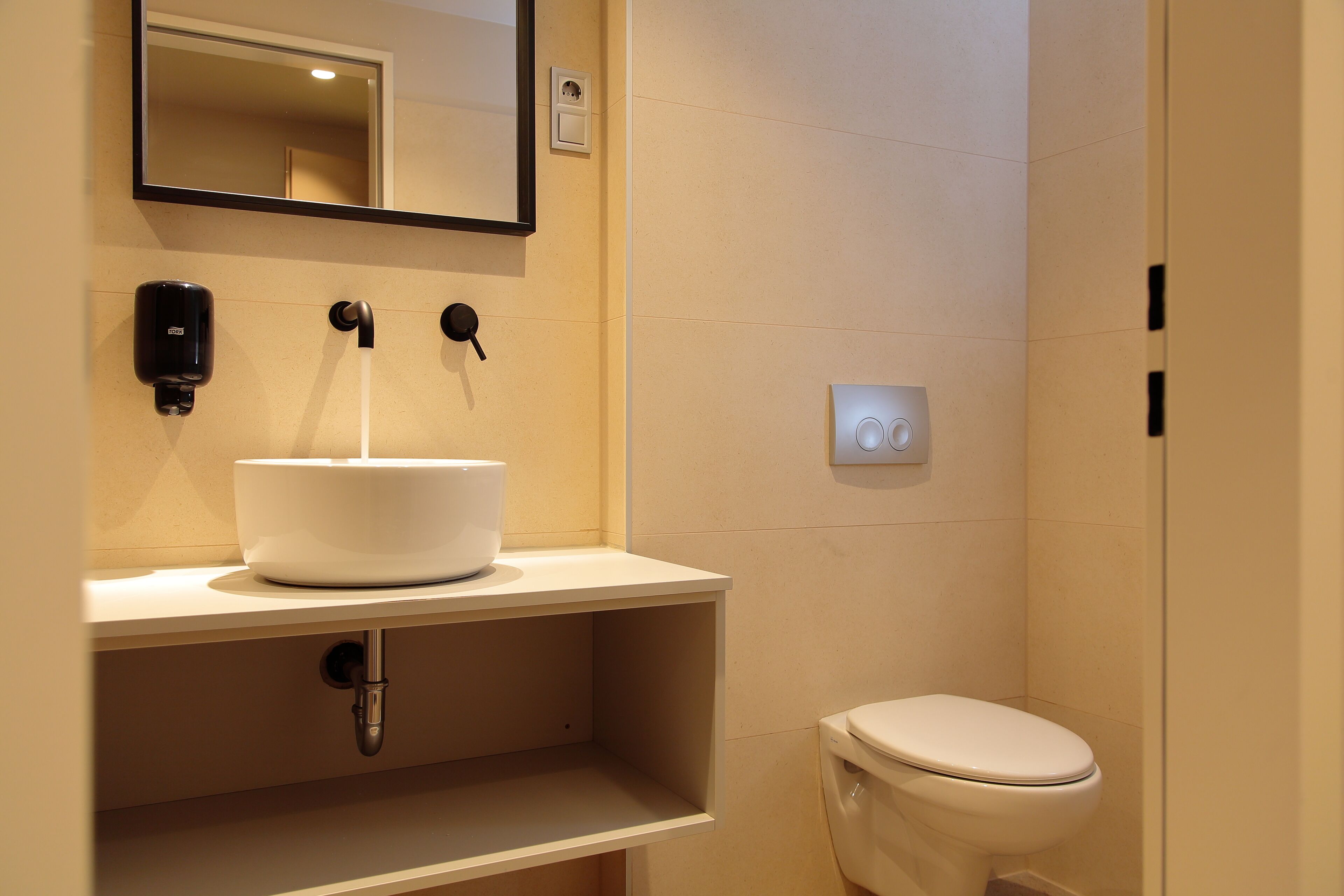 Un baño moderno con un lavabo blanco, un espejo encima, un inodoro y un interruptor de luz en la pared.