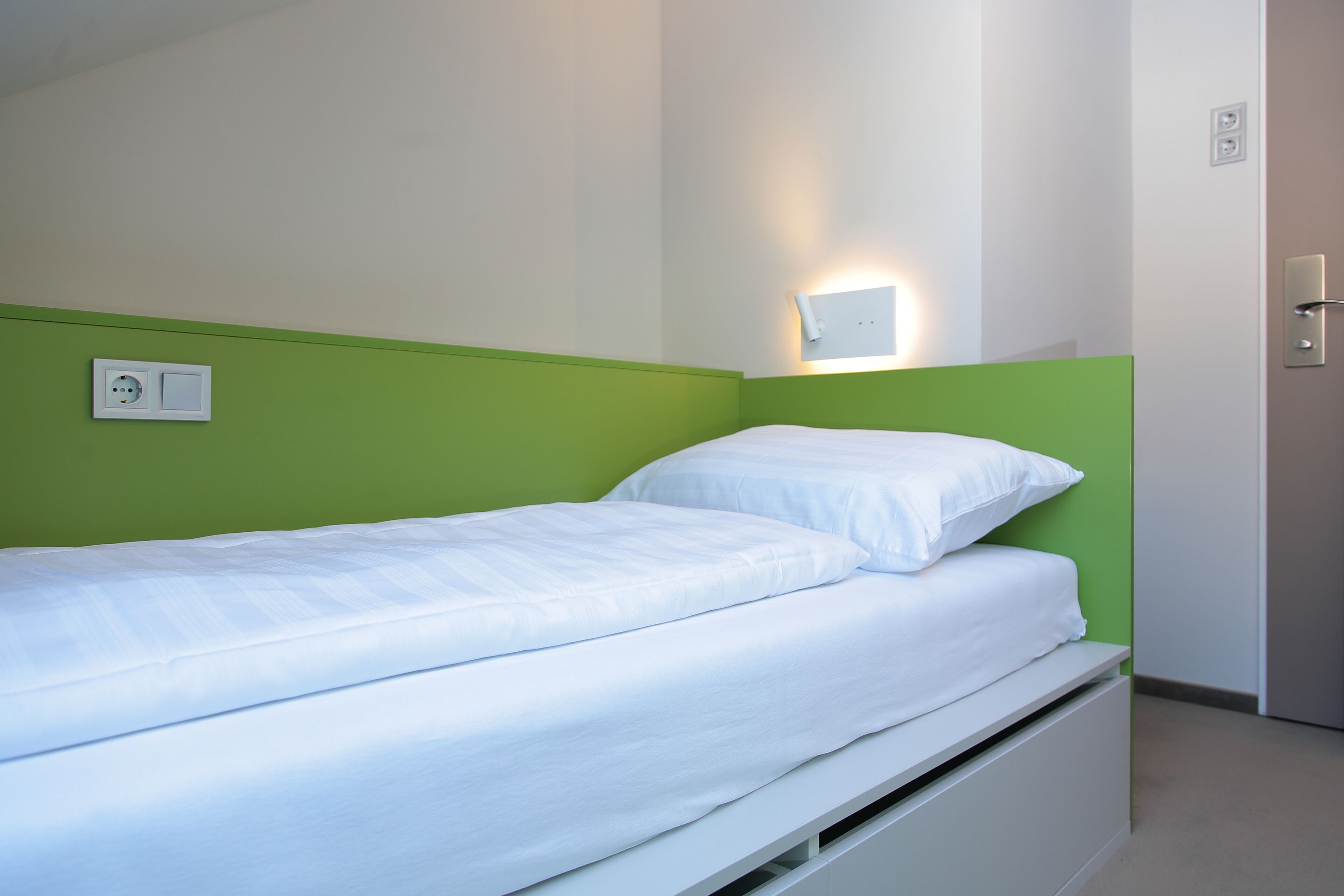A single bed with white bedding in a room with green walls and a white headboard.