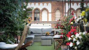 An outdoor seating area with wicker furniture, a grey sofa, and a table with a potted plant. - Maverick Central Market (Budapest)