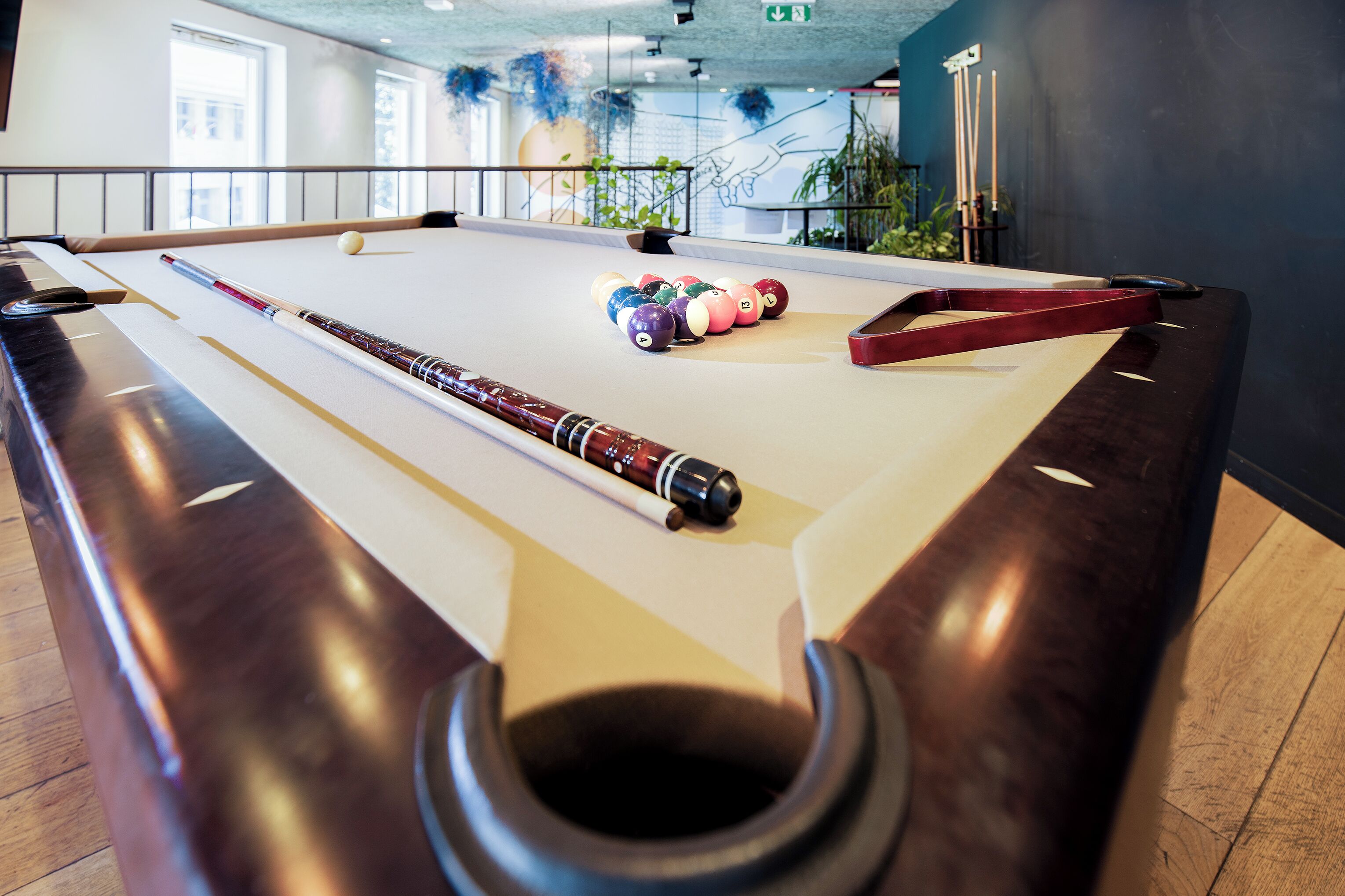 A pool table with a pool cue, balls, and a red bridge.
