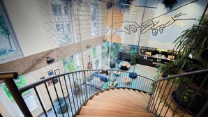 A spiral staircase with a wooden finish and metal railings, leading to a lower level with a seating area and a mural on the wall. - Maverick Central Market (Budapest)
