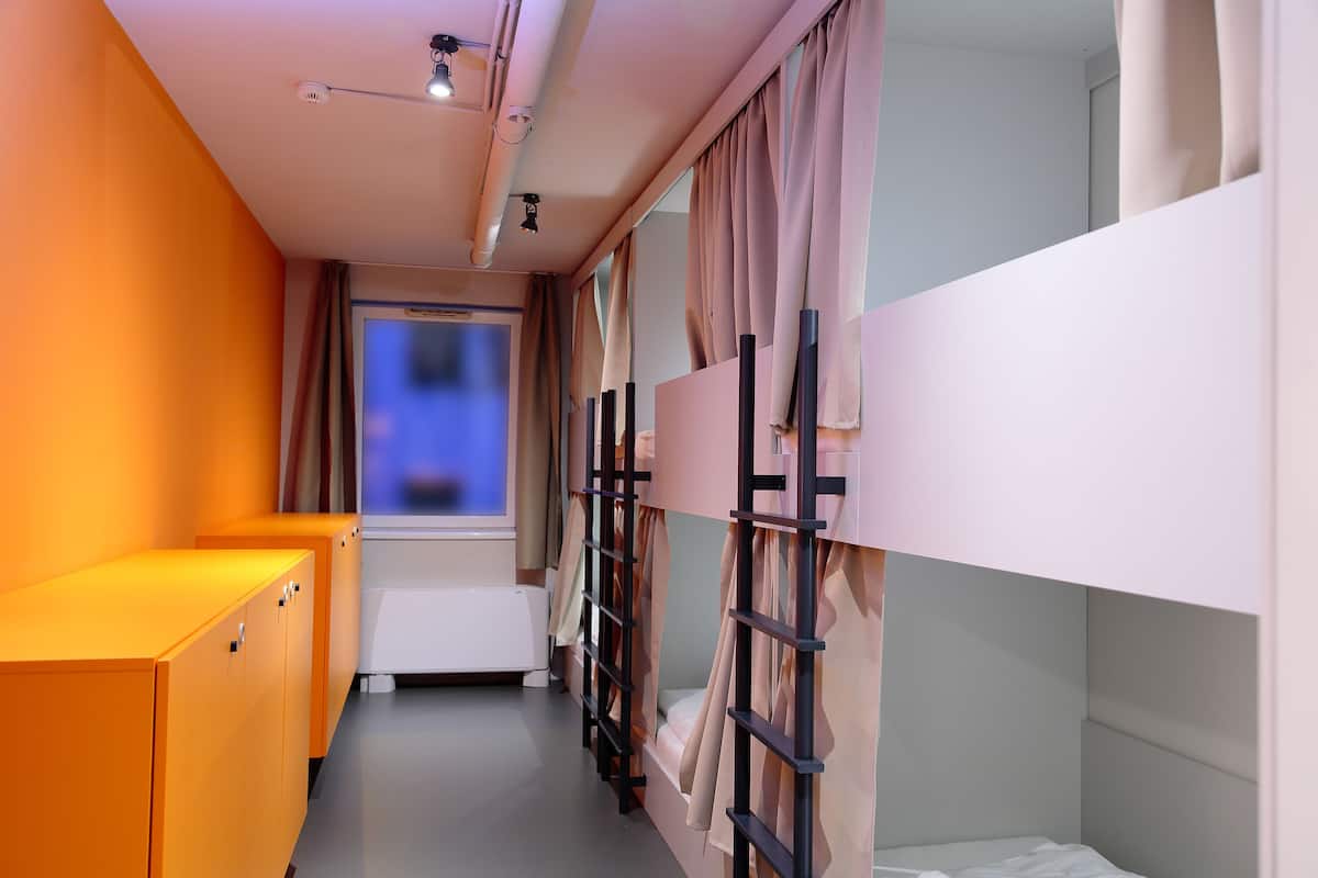 Un couloir étroit avec des lits superposés, une fenêtre et un radiateur.