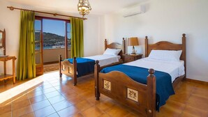 A hotel room with two wooden beds, a balcony with green curtains, a wooden floor, and a chandelier. - Villa overlooking the Port of Andratx with private pool (Port D'Andratx)