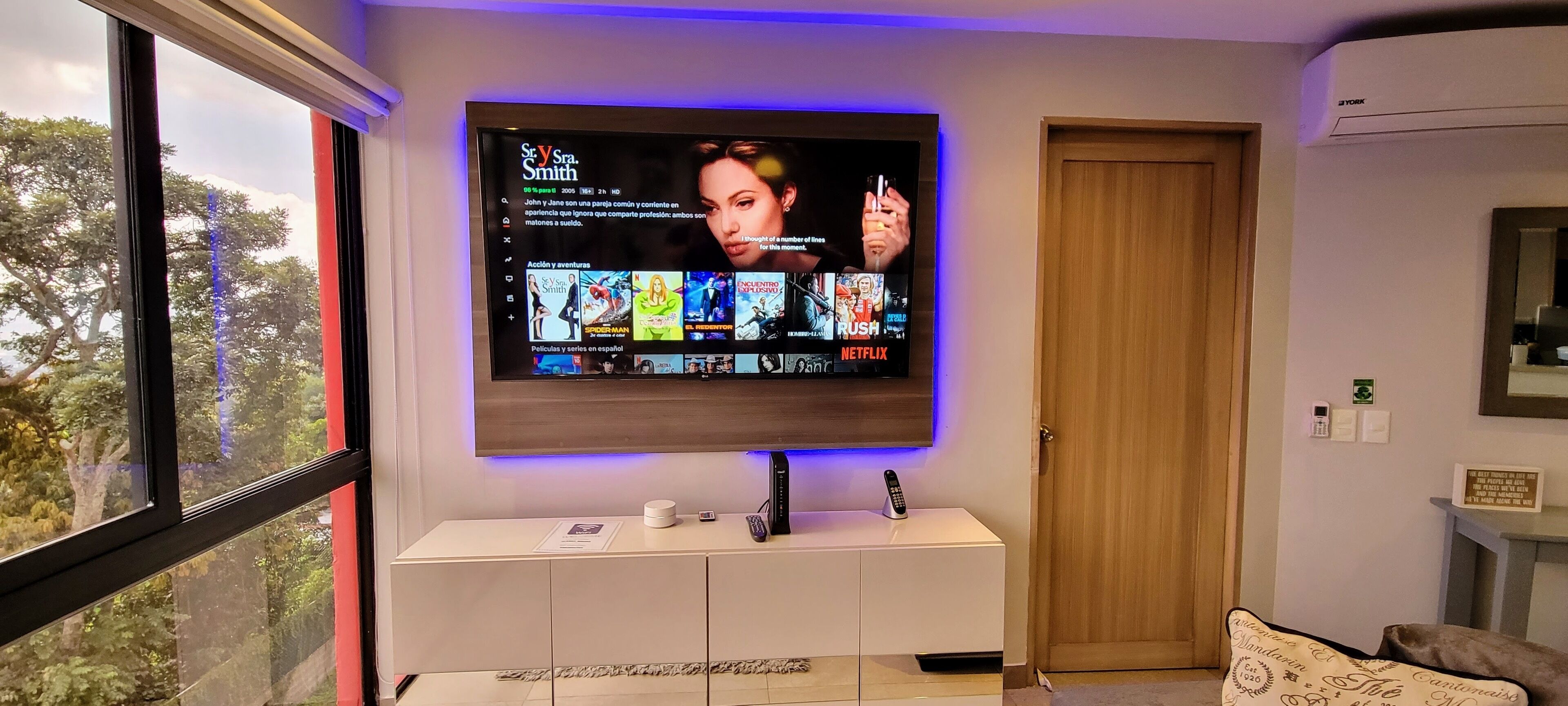 A flat-screen TV mounted on a wall with a selection of movies and TV shows displayed.