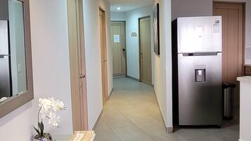 Un pasillo con un refrigerador, un cesto de basura y un banco con una orquídea en maceta.