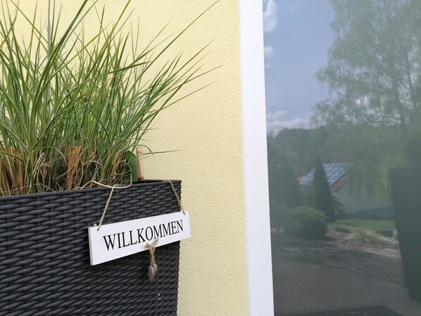 Ein Korbbasket mit einem 'WILLKOMMEN'-Schild, einer Pflanze und Blick auf eine Straße und Bäume.