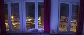 A room with large windows, a view of the cityscape, and red curtains. - Guesthouse 4Roomz (Bologna)
