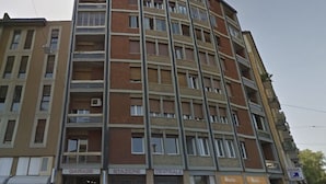 A multi-story building with a curved facade, featuring ground-floor commercial spaces including a garage, a self-service tobacco shop, and a central area. - Guesthouse 4Roomz (Bologna)