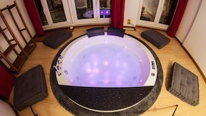 A circular hot tub with a control panel, surrounded by wooden flooring and four cushioned seating areas. - Guesthouse 4Roomz (Bologna)