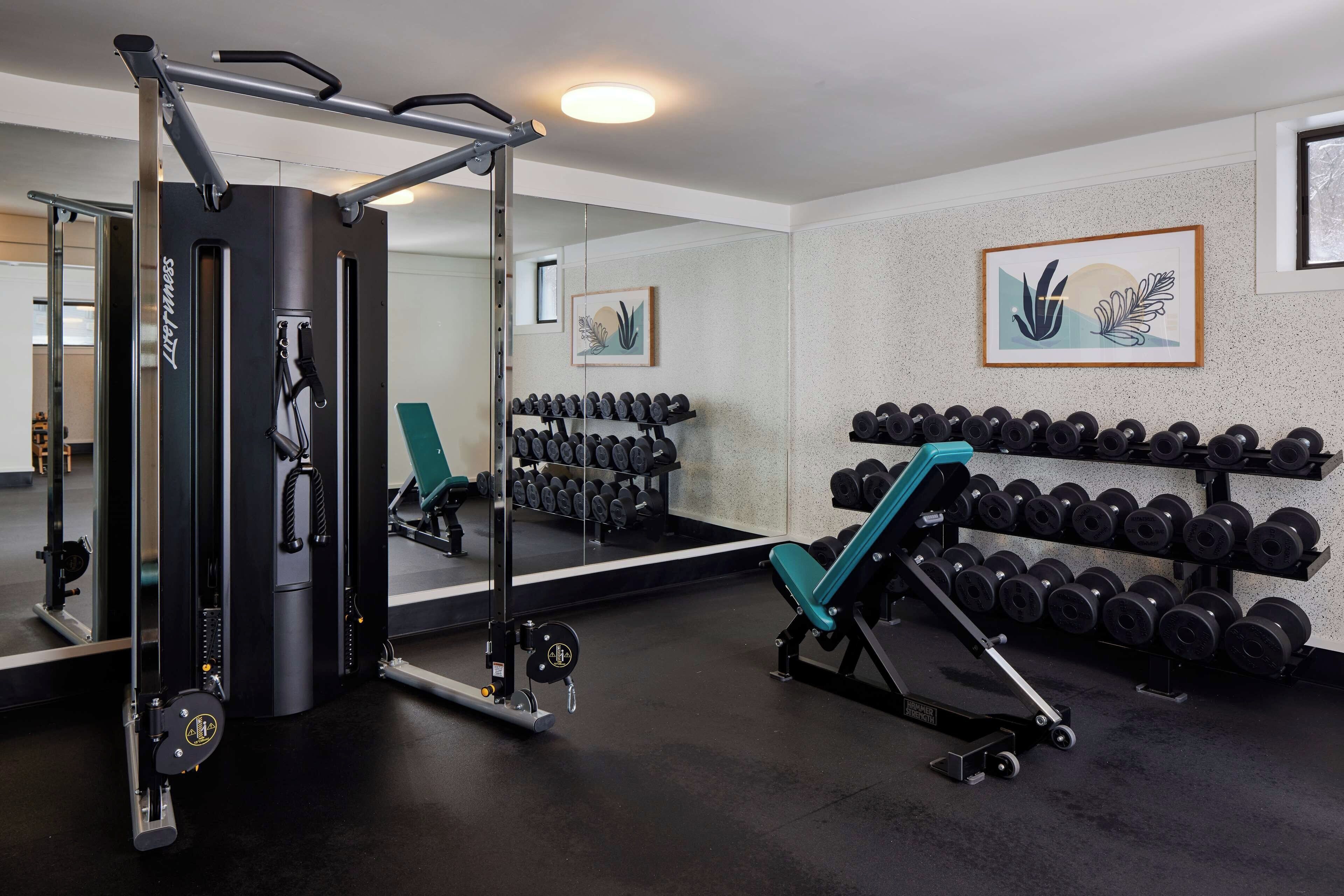 A gym with exercise equipment, a mirror, and a wall with framed artwork.