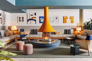 A modern living room with a central glass-top fireplace, striped sofas, and abstract wall art. - Wayfinder Newport (Newport)