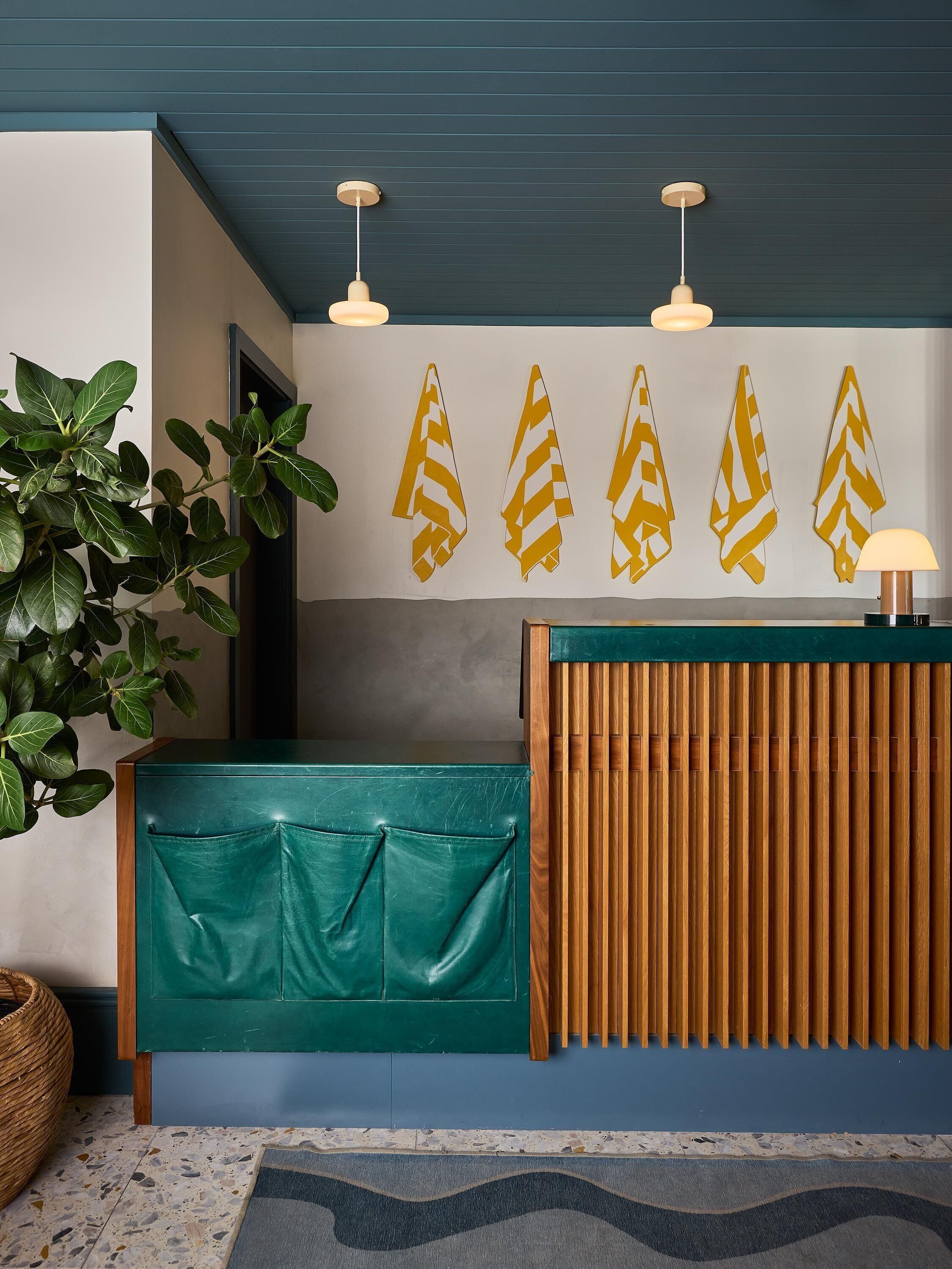 Un espace d’accueil avec un comptoir vert, un lambris en bois et une plante.