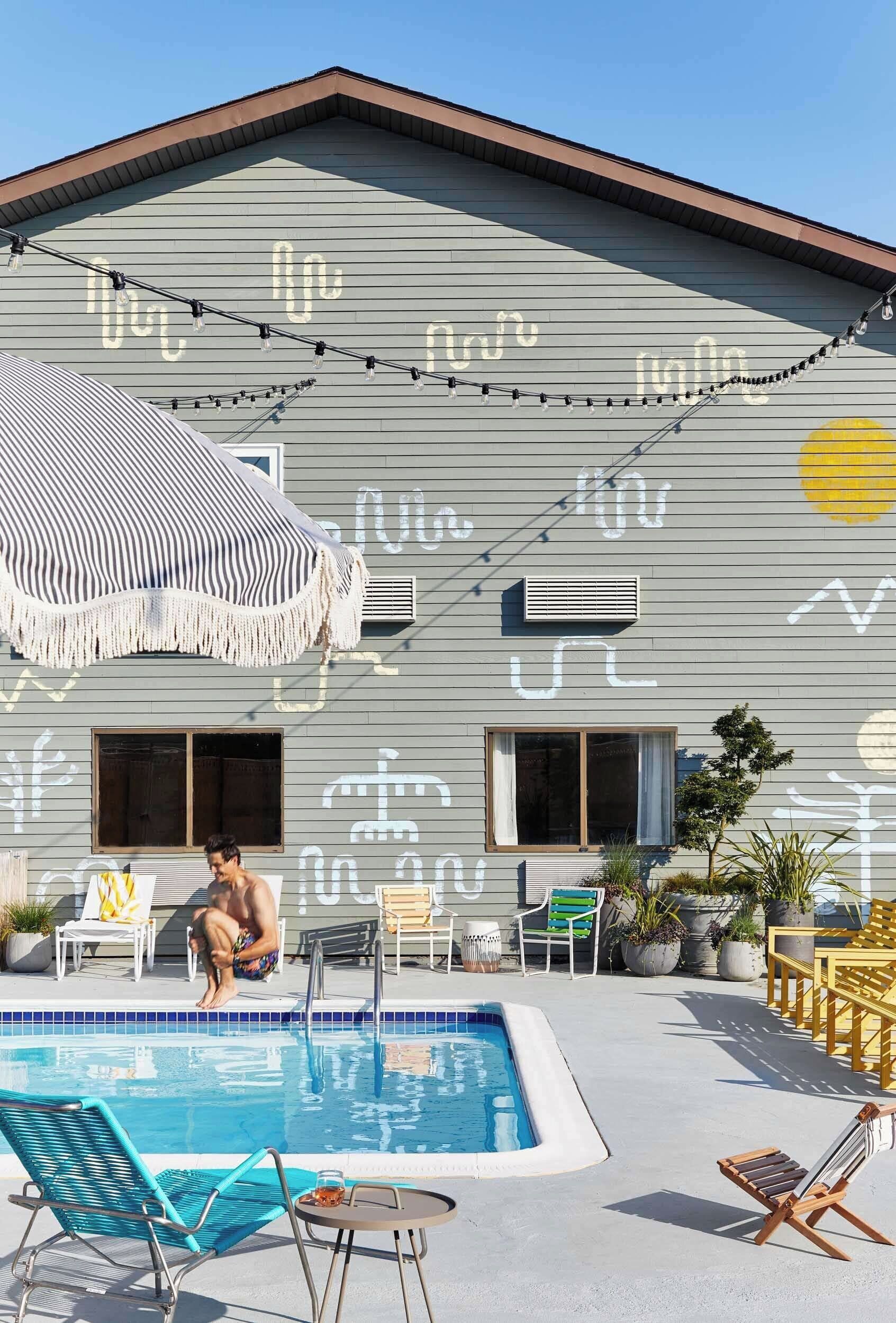 A pool area with lounge chairs, a small table, and a person sitting by the pool.