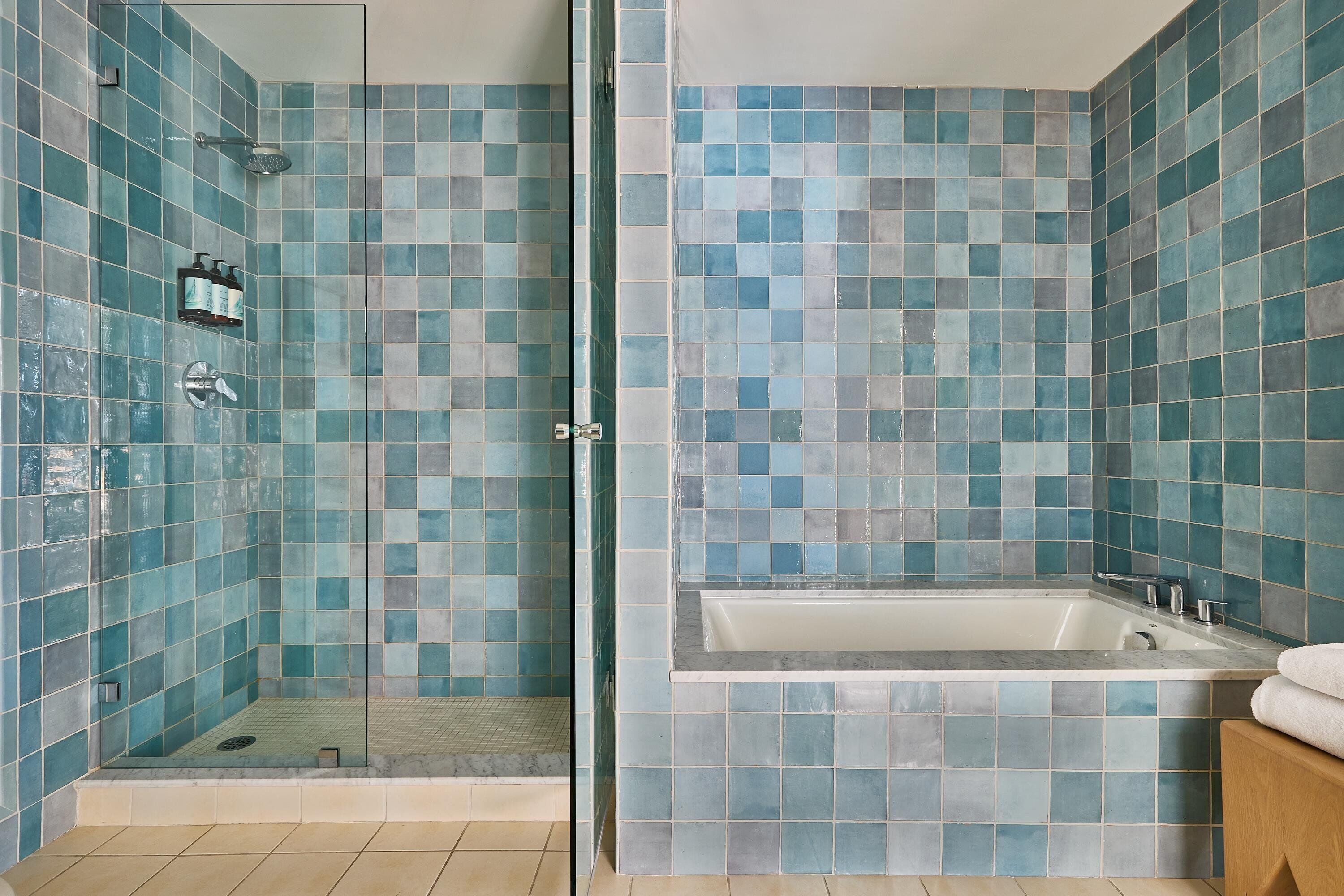 A bathroom with a glass-enclosed shower, a bathtub, and a tiled wall.