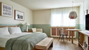 Habitación de hotel con cama, escritorio, silla, lámpara, televisor y obras de arte en la pared.