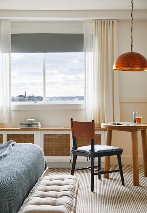 Hotelkamer met een bed, een stoel, een tafel met een drankje, en uitzicht op de stad door het raam.