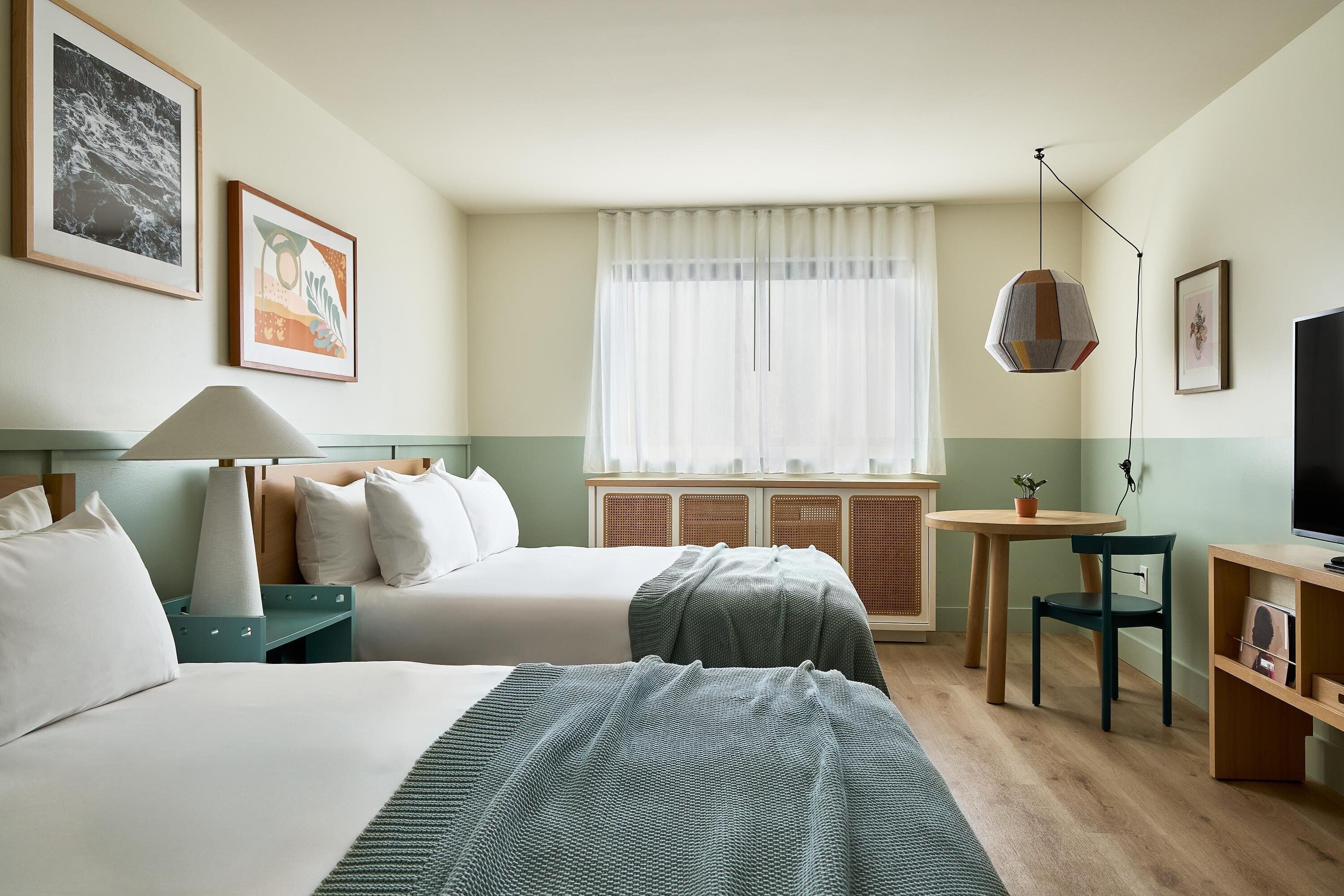 Habitación de hotel con dos camas, un escritorio, una silla, un televisor y una ventana con cortinas.