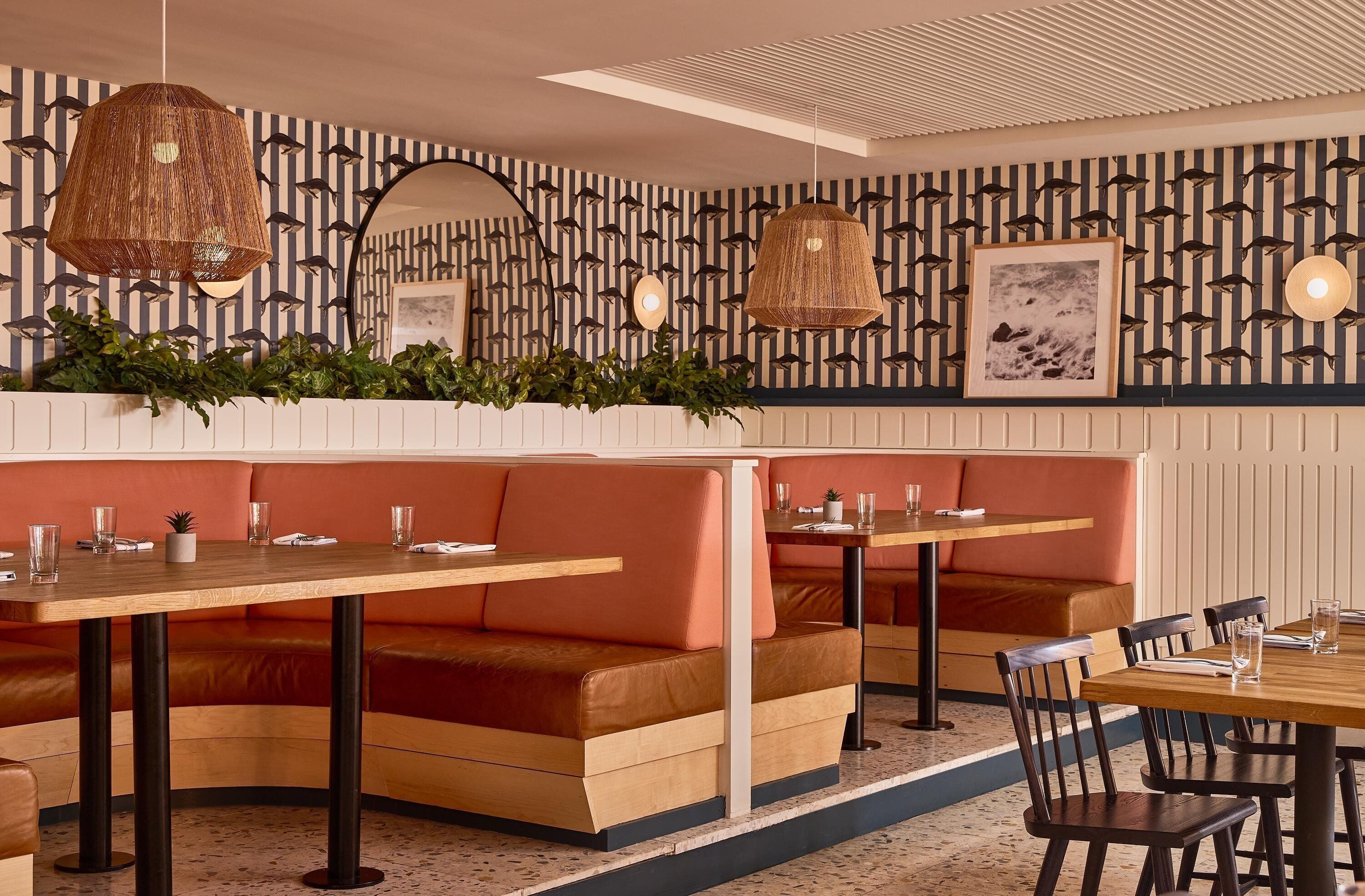Interior de restaurante con asientos tipo cabina, mesas y lámparas de mimbre colgantes.