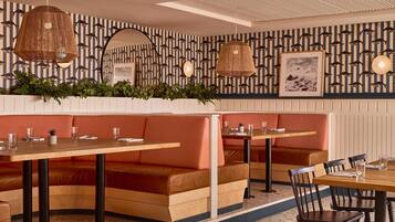 Interior de restaurante con asientos tipo cabina, mesas y lámparas de mimbre colgantes.
